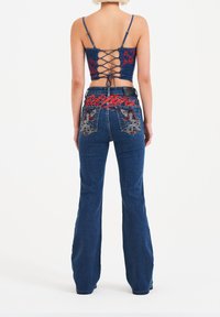 Blå denim flared jeans med detaljeret rød og hvid broderi på baglommerne; parret med en navy crop top med snørebåndsdesign bagpå.