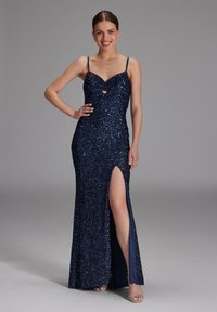 Robe de soirée en sequins bleu marine avec une silhouette ajustée, un décolleté en V, une fente latérale et des bretelles spaghetti ajustables. Présente un détail en trou de serrure au niveau de la poitrine.