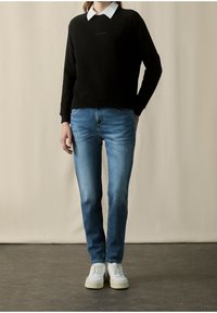 Czarna bluza z białym kołnierzem, niebieskie dżinsy i białe sneakersy. Gładka faktura, luźny krój i kontrastujące kolory.