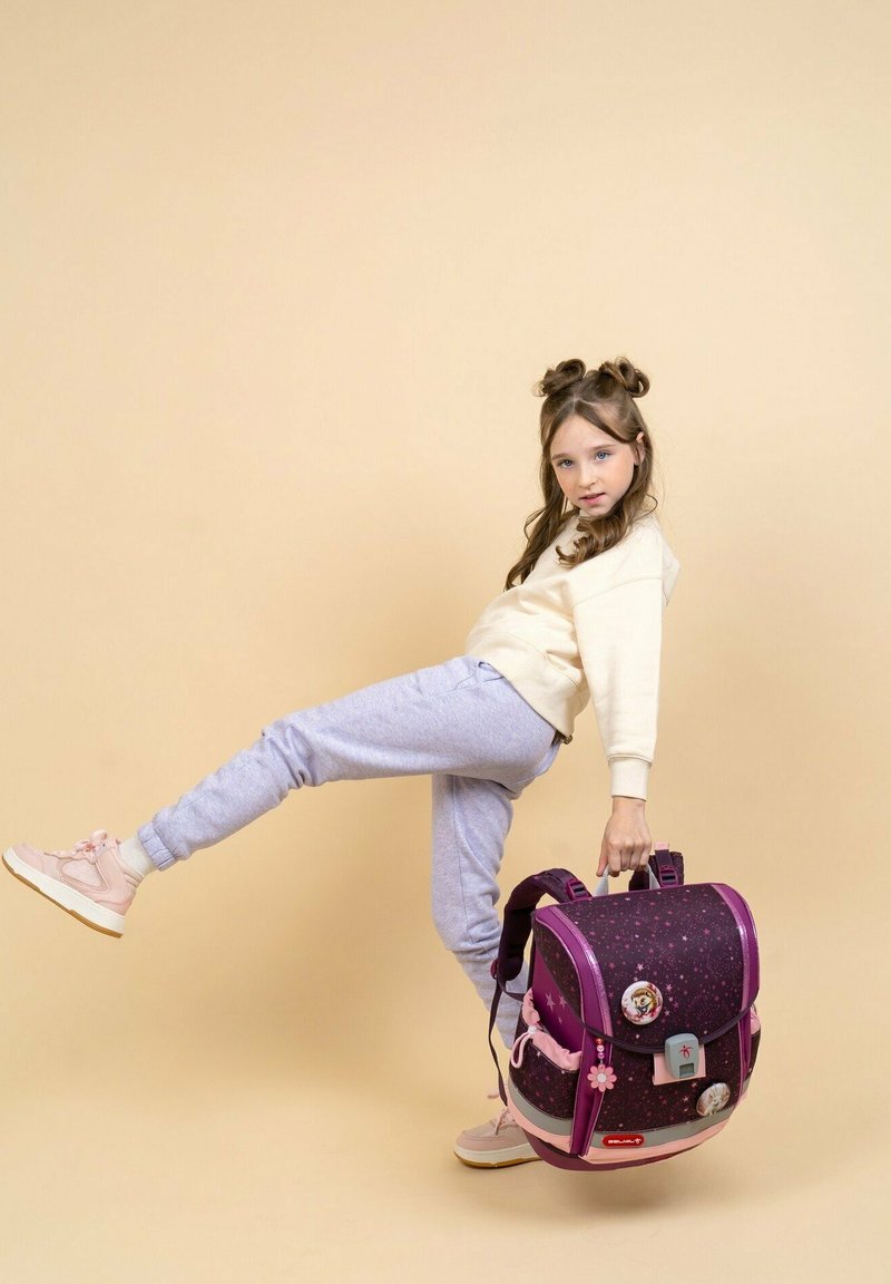 Zaino viola e rosa con motivo a stelle, spallacci regolabili, tasca frontale e decorazioni. Ragazza in posa mentre lo tiene.