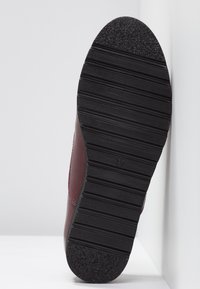 Chaussure en cuir bordeaux avec une semelle en caoutchouc noire texturée, comportant des rainures horizontales pour l'adhérence et un design de bout arrondi.