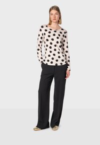 Maglietta a maniche lunghe color crema con pois neri, abbinata a pantaloni neri a gamba larga; modello che indossa scarpe metallizzate. Design semplice, texture morbida.