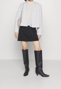 Světlý šedý umělý kožíšek s prošívaným vzorem, zkombinovaný s béžovým tričkem, černou mini sukní a dlouhými černými koženými botami na podpatku.