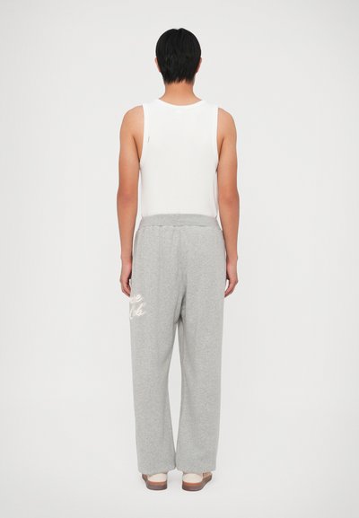 Grijze sweatpants met een losse pasvorm, elastische tailleband, met een witte grafische accent. Gecombineerd met een mouwloos wit tanktop.