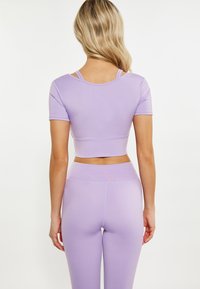 Top sporty de culoare violet deschis, cu mâneci scurte, fabricat dintr-un material neted, cu detalii cu dantelă la spate, asortat cu leggings corespunzători.