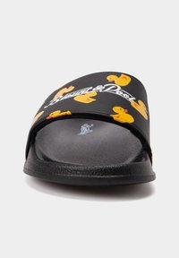 Black slide sandal with a matte finish, featuring a yellow rubber duck pattern and white logo on the strap; textured footbed for grip.