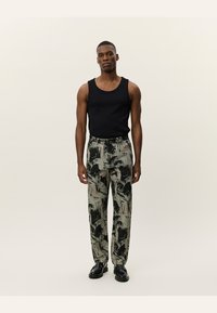 Black tank top, patterned grey and green trousers, tailored fit, and black shoes. The trousers feature abstract brushstroke designs.