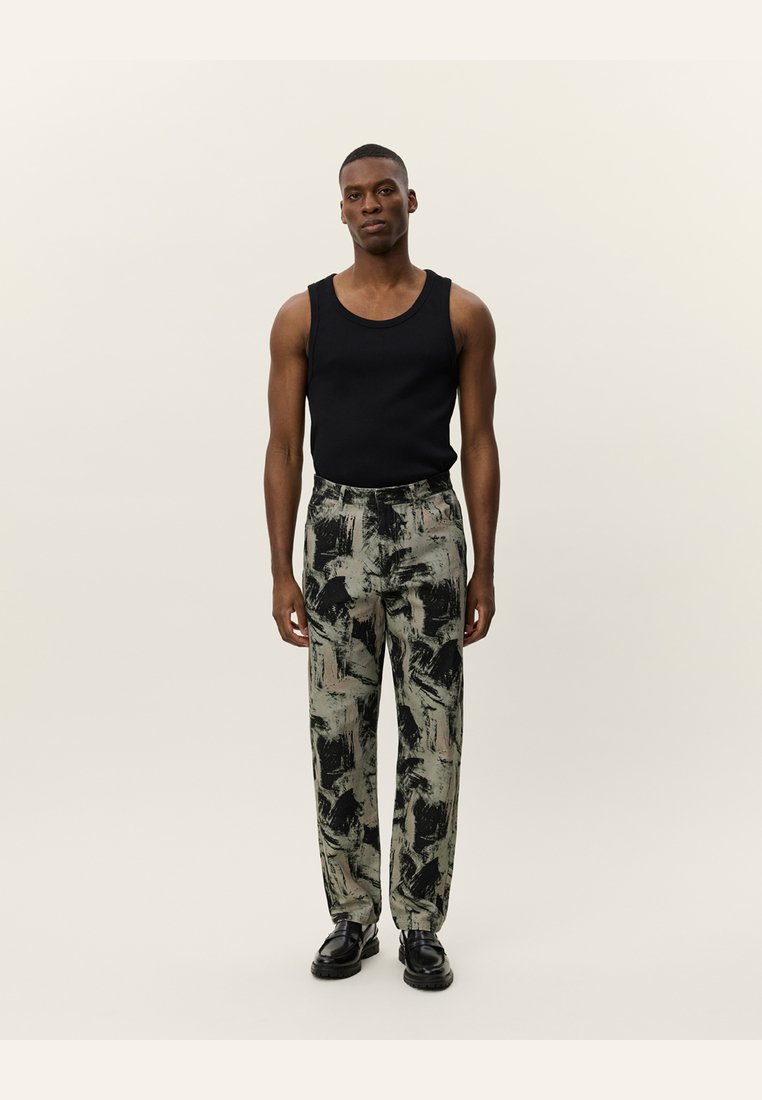 Black tank top, patterned grey and green trousers, tailored fit, and black shoes. The trousers feature abstract brushstroke designs.