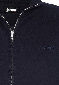 Granatowy sweter na zamek wykonany z fakturowanej dzianiny. Posiada wysoki kołnierz, srebrny zamek oraz dyskretny niebieski logo na lewej piersi.