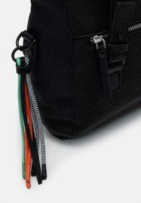 Czarna teksturowana torba z zamkiem błyskawicznym, regulowanym paskiem oraz kolorowymi sznurkami w odcieniach zieleni, pomarańczy, czerwieni i czerni z wzorzystymi detalami.