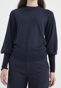 Granatowy dzianinowy sweter z wysokim kołnierzem, rękawami raglanowymi oraz ściągaczami na mankietach i dole. Miękka tekstura o luźnym kroju.