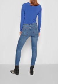 Top azul de manga larga combinado con jeans ajustados de talle medio en azul que cuentan con dos bolsillos traseros y un dobladillo deshilachado, con botas negras hasta el tobillo.