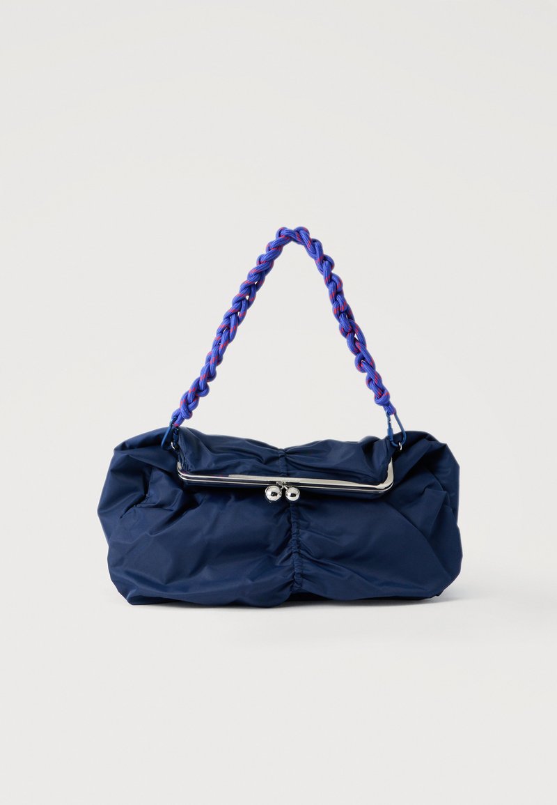 Marineblaue Handtasche aus gerafftem Stoff mit silbernem Verschlussrahmen und geflochtenem blau-rotem Riemen, präsentiert vor weißem Hintergrund.