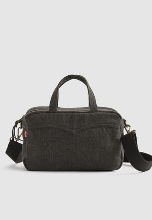 Zwarte stoffen tas met twee korte handvatten, een afneembare schouderriem en ritssluiting. Kenmerkt zich door subtiele stiksels en een logo-tag.