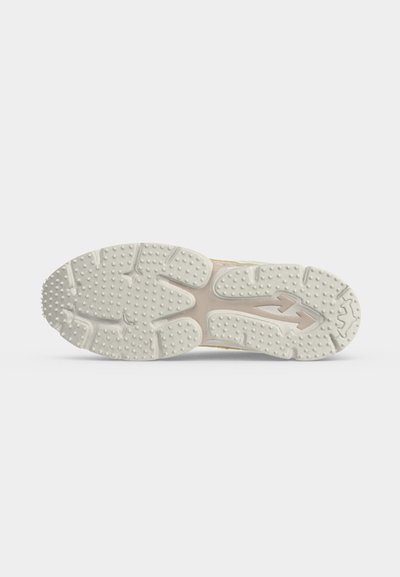 Semelle d'une basket beige avec des points de grip texturés et des rainures pour la traction, présentée sur un fond blanc uni.