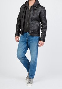 Zwarte leren jas met ritszakken, grijze capuchontrui eronder, blauwe spijkerbroek en grijze sneakers. Soepele textuur en aansluitend ontwerp.