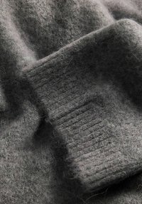 Grå ulltyg med en mjuk, fluffig textur, som har en ribbad stickad del. Materialet verkar lätt tovigt, vilket skapar en lagerliknande effekt.