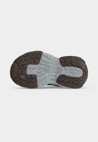 Semelle de chaussure avec une bande de roulement en caoutchouc noir et gris comportant des motifs texturés pour la traction sur fond blanc.