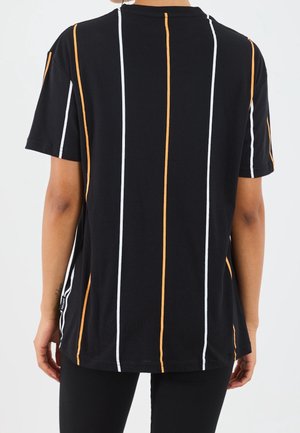 Persoon die een zwart shirt met korte mouwen draagt met verticale witte en oranje strepen, gezien van achteren, met ontspannen armen langs het lichaam.