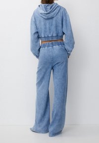 Sudadera recortada de mezclilla azul clara con cinturilla y puños elásticos, combinada con pantalones de talle alto y holgados que cuentan con una banda elástica.