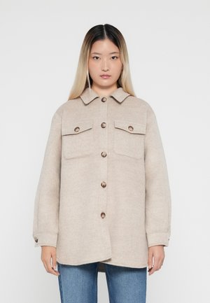 Veste chemise en laine beige avec un col, deux poches avant et une fermeture à boutons ; présente une coupe décontractée et un tissu texturé.