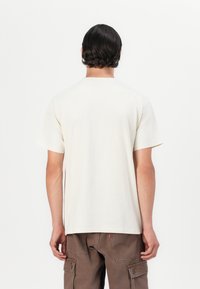 Kremfarget t-skjorte med korte ermer og rund hals, laget av mykt stoff. Baksiden har et minimalistisk design uten grafikk eller mønstre.