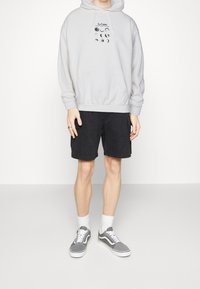 Grå hoodie med grafiskt tryck och en framficka, tillsammans med svarta cargoshorts och grå sneakers. Vita strumpor synliga.