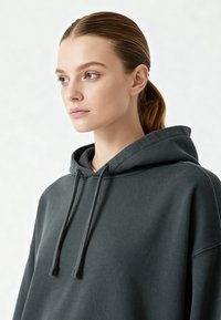 Felpa grigia scura con cappuccio regolabile, realizzata in tessuto morbido. Presenta una vestibilità ampia e un cappuccio foderato. Design minimalista senza motivi visibili.