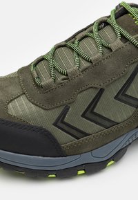 Grüner Sportschuh mit einer Mischung aus strukturiertem Stoff und Wildleder, ausgestattet mit schwarzen Akzenten und lebhaften grünen Schnürsenkeln, verstärkter Zehenkappe und gepolsteter Sohle.