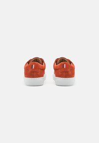 Suede orange sneakers with white rubber soles. Back view showing rounded collar, red and blue accent stripes near heel.