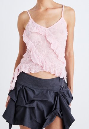 Modèle portant un caraco en dentelle rose pâle avec une bordure à volants et une jupe bleu marine foncé à volants.