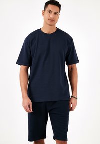 Tricou bleu marine cu mânecă scurtă, cu decolteu rotund și manșete răsucite, asortat cu pantaloni scurți dintr-un material moale, texturat.