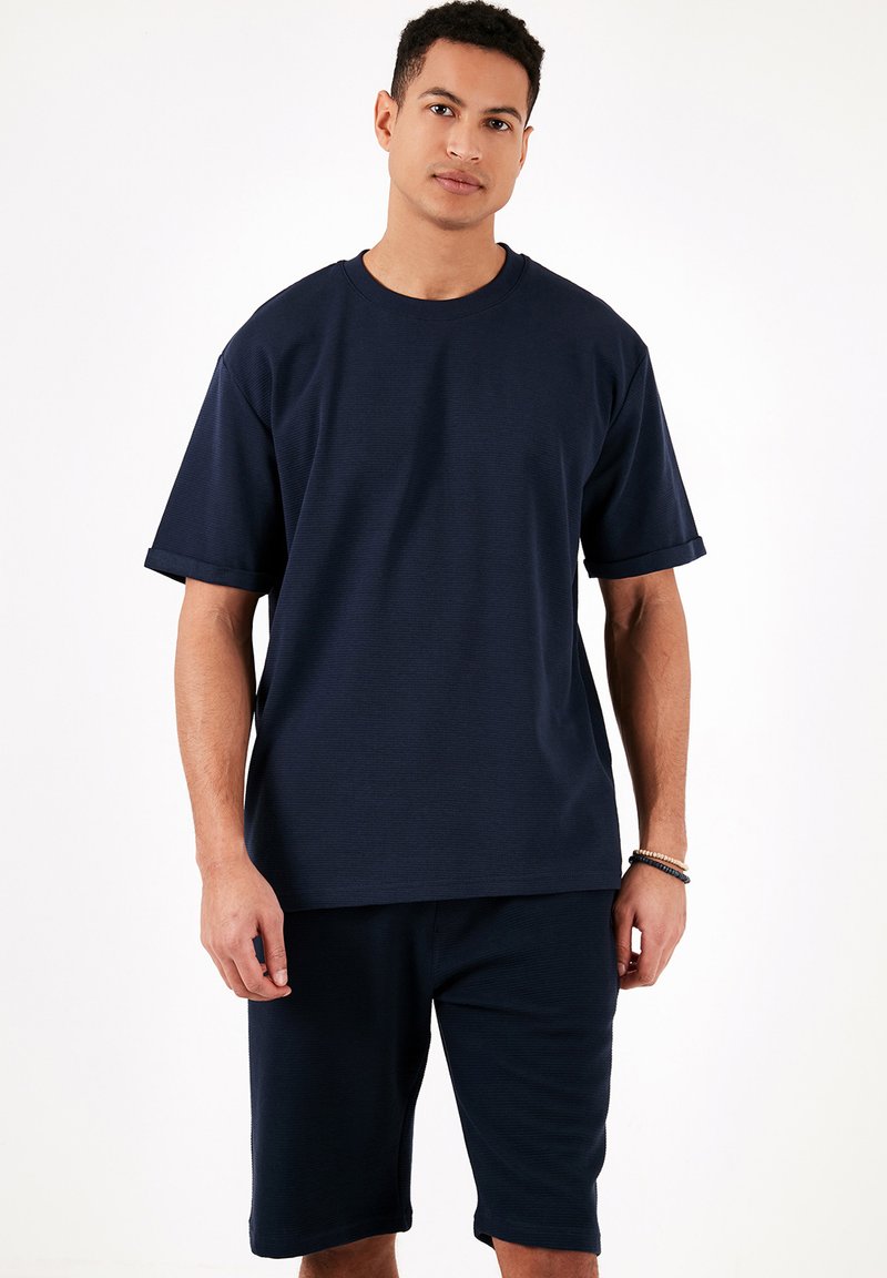 Tricou bleu marine cu mânecă scurtă, cu decolteu rotund și manșete răsucite, asortat cu pantaloni scurți dintr-un material moale, texturat.