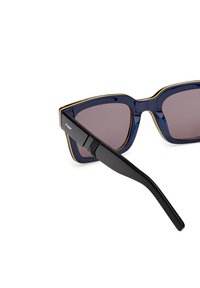 Occhiali da sole a forma di occhio di gatto con una montatura blu navy, accentuati da dettagli dorati e lenti scure; le stanghette nere sottili presentano un design testurizzato vicino alla cerniera.