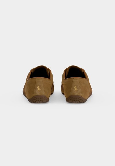 Ζευγάρι καφέ σουέντ παπούτσια τύπου slip-on με μικρό χρυσό λογότυπο αλόγου στη φτέρνα, εμφανιζόμενα από πίσω σε απλό φόντο.