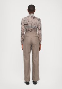 Doorzichtige blouse met lange mouwen in een lichtbeige abstract patroon, gecombineerd met hoge taille, bruin en crèmekleurige houndstooth wijde broek.