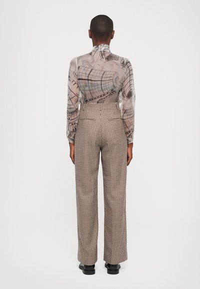 Durchsichtige Bluse mit langen Ärmeln und einem hellbeigen abstrakten Muster, kombiniert mit hochtaillierten, braun-creamfarbigen Hahnentritt-Hosen mit weitem Bein.