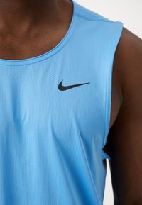 Personne à la peau foncée portant un débardeur de sport Nike bleu clair avec un logo Nike noir sur la poitrine.