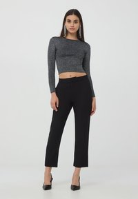 Szary prążkowany krótki top z długim rękawem, zestawiony z czarnymi dopasowanymi spodniami i czarnymi szpilkami. Modelka nosząca wyraziste kolczyki.