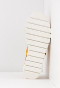 Semelle de chaussure avec une base en caoutchouc blanc et des cannelures texturées, complétée par un panneau latéral jaune. Le design est large et robuste.