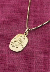 Goldanhänger an einer Kette, mit einer geprägten Figur, die von Sternen umgeben ist, ovale Form und polierte Oberfläche, vor einem strukturierten lila Hintergrund.