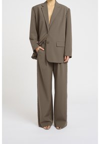 Blazer oversize marron avec clous sur les côtés, pantalon large assorti avec des accents festonnés. Tissu doux et lisse avec une coupe décontractée.