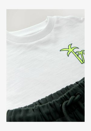 White sweatshirt with round neckline and light green palm tree graphic. Below, dark green elastic waistband of matching sweatpants with drawstring.