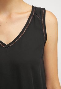 Top senza maniche nero con scollatura a V e dettagli in pizzo lungo i bordi, realizzato in tessuto liscio.