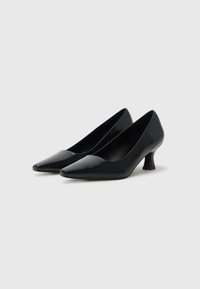 Zapatos de charol negro con puntera afilada y un tacón corto y único en bloque. Textura lisa con un diseño elegante y sin adornos visibles.