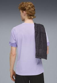 Tricou sportiv de culoare violet deschis cu mâneci cu model și un prosop închis la culoare aruncat pe umăr. Textură netedă și croială comodă.