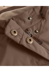 Veste imperméable marron avec un col montant, comportant des éléments en métal doré, une poche zippée sur le côté et une doublure douce de couleur crème.
