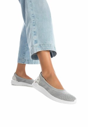 Zapatos grises sin cordones con parte superior de punto texturizado, suela blanca y detalles metálicos. Combinados con jeans cortos de color azul claro.