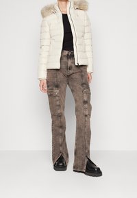 Valkoinen toppatakki tekoturkistakilla, musta paita ja ruskeat cargo-housut, joissa on halkiot lahkeissa, yhdistettynä mustiin paksupohjaisiin saappaisiin.