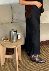 Czarna satynowa sukienka maxi, brązowy dziany kardigan, skórzane botki z wężowym wzorem na kostkę, srebrny stalowy dzbanek do kawy, drewniany stołek z przekąskami.